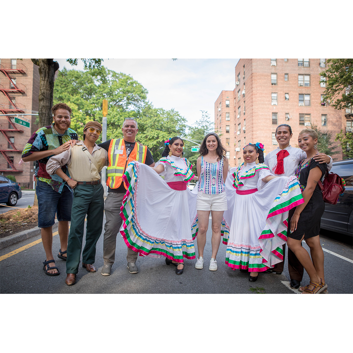 34th Avenue Oral History participants pose for a photo on the Open Street after the launch event. Narrators Manuela Agudelo, Jim Burke, and Erick Modesto stand with oral historian Bridget Bartolini and dancers from Ballet Folklorico Nueva Juventud, who are wearing traditional Mexican costumes.
